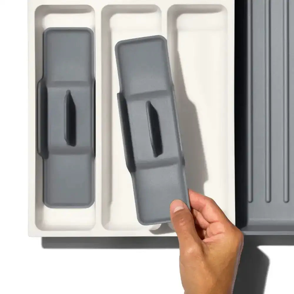 Gray kitchen cabinet door handles being installed on a white cabinet with a hand assisting.