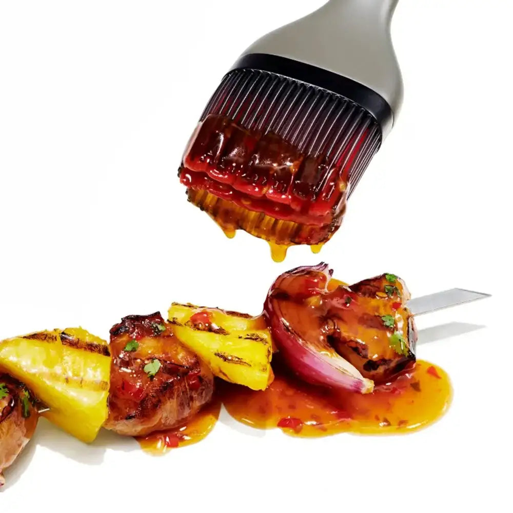 Barbecue brush applying sauce to skewered meat and pineapple on a white background