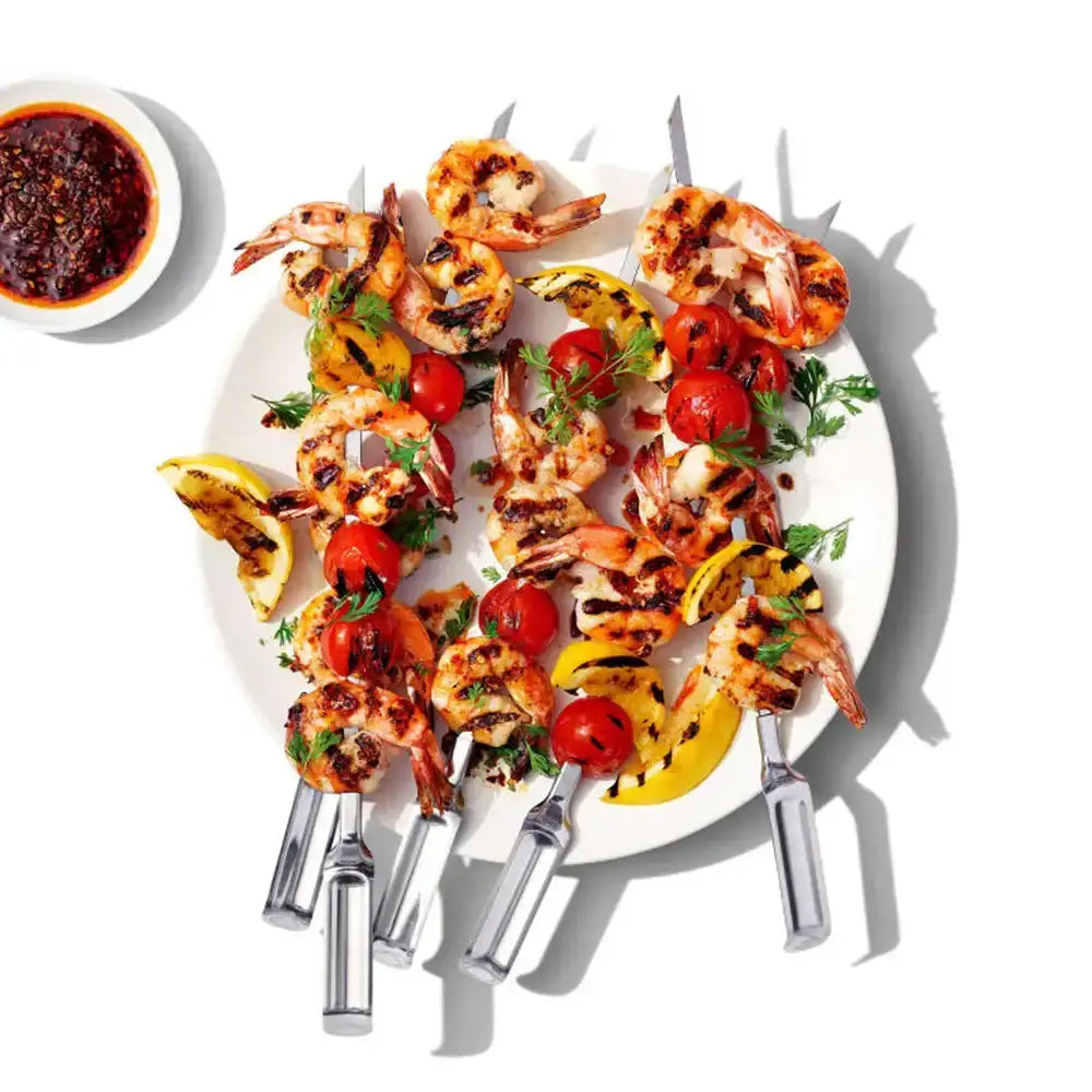 Grilled shrimp skewers with vegetables on a white plate with a side of sauce.