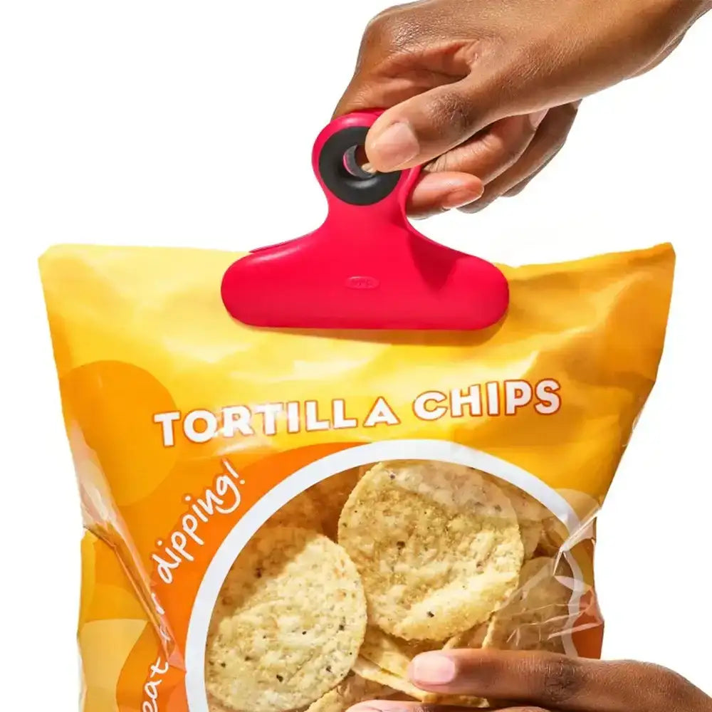 Hand holding a bag of tortilla chips with a red clip
