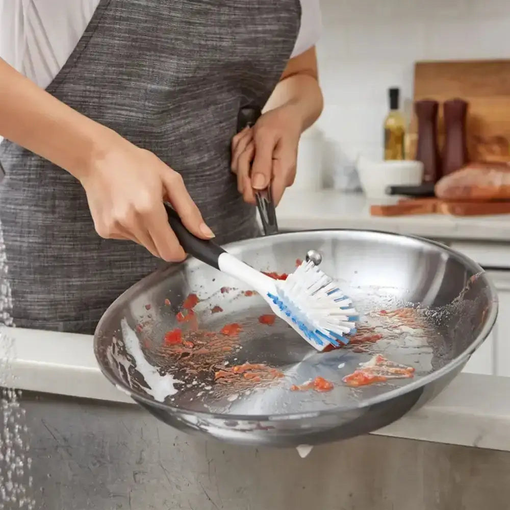 Person cleaning a frying pan with a brush in a kitchen setting