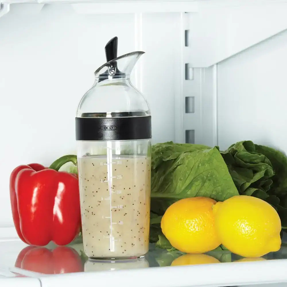 Clear bottle with black cap on a refrigerator shelf with vegetables and lemons