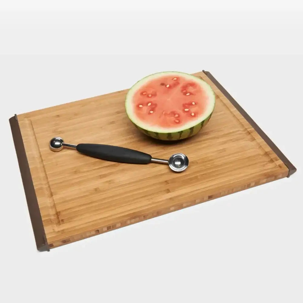 Half-cut watermelon on a wooden cutting board with a melon baller.