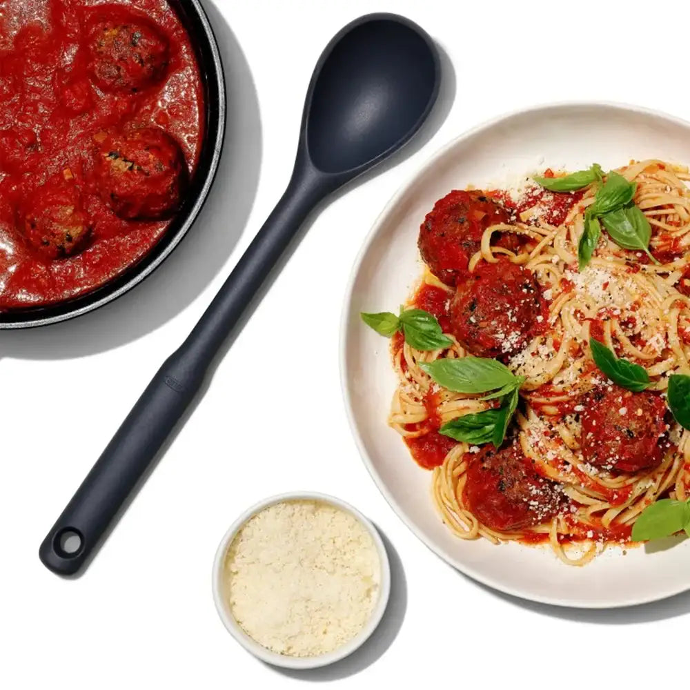 Spaghetti with meatballs on a plate, pan of meatballs, and bowl of parmesan cheese.
