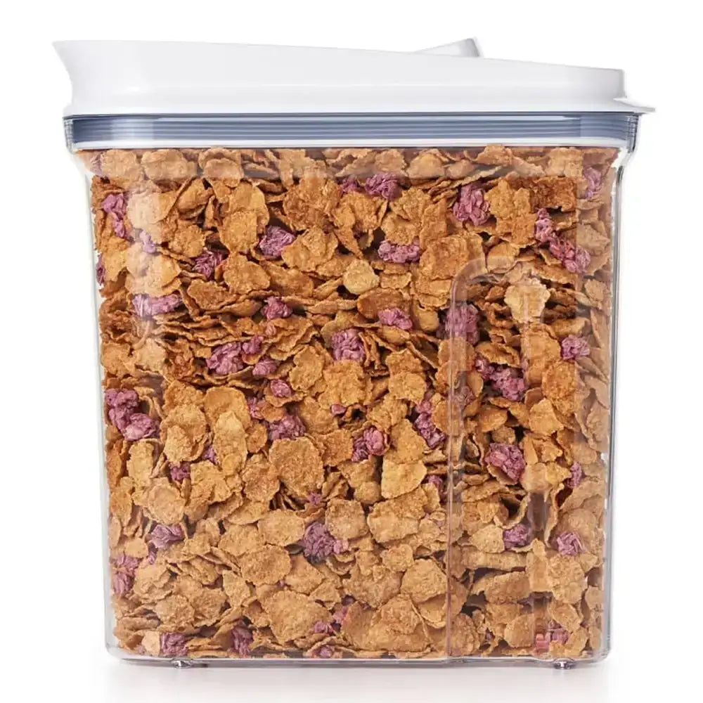 Clear container filled with cereal and pink berries on a white background