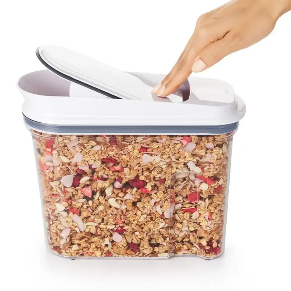 Container of granola with a hand opening the lid on a white background