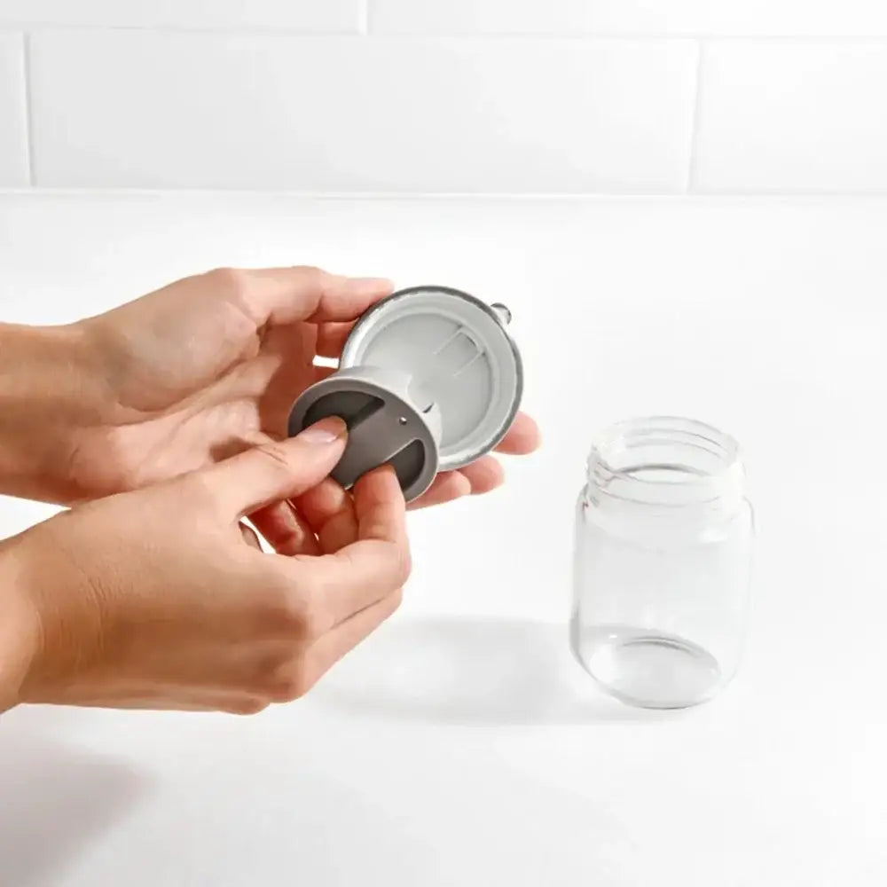 Person holding a metal lid over a glass jar on a white background