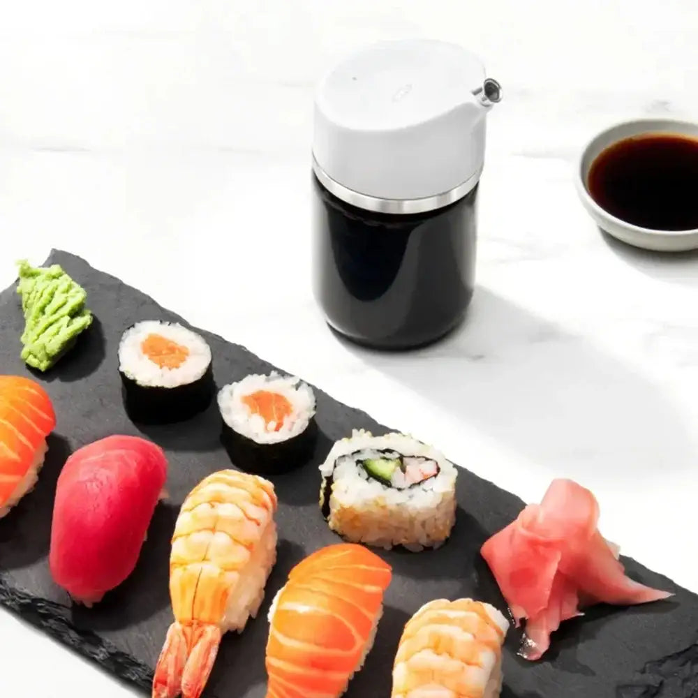 Assorted sushi on a black slate with a soy sauce container and wasabi.