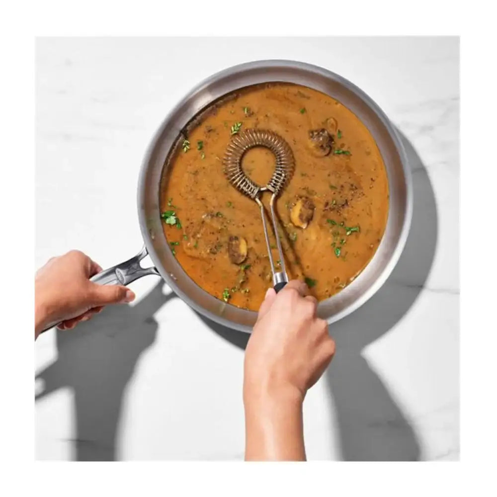 Person holding a frying pan with a creamy dish and a whisk.