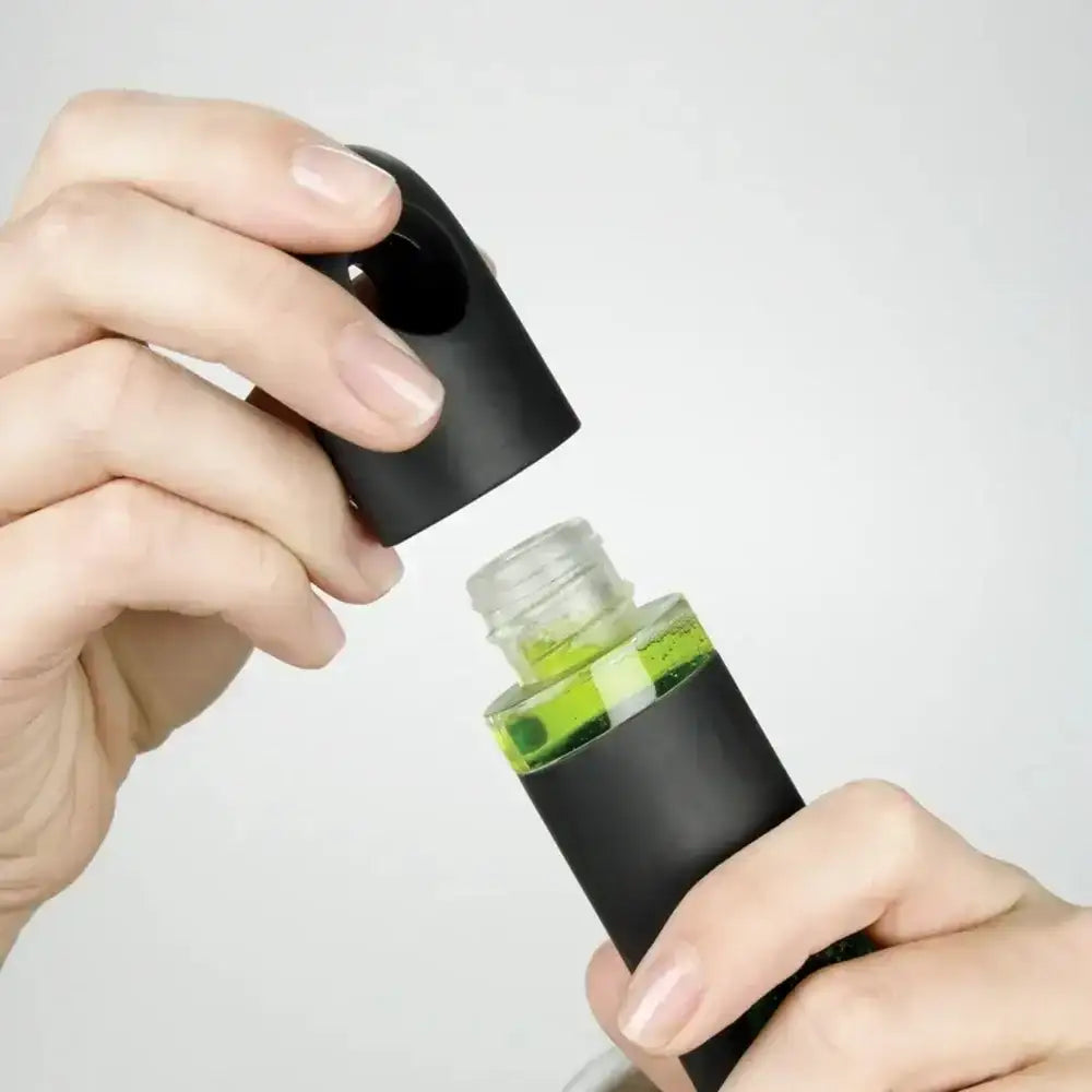 Person holding a black spray bottle with a clear cap against a white background