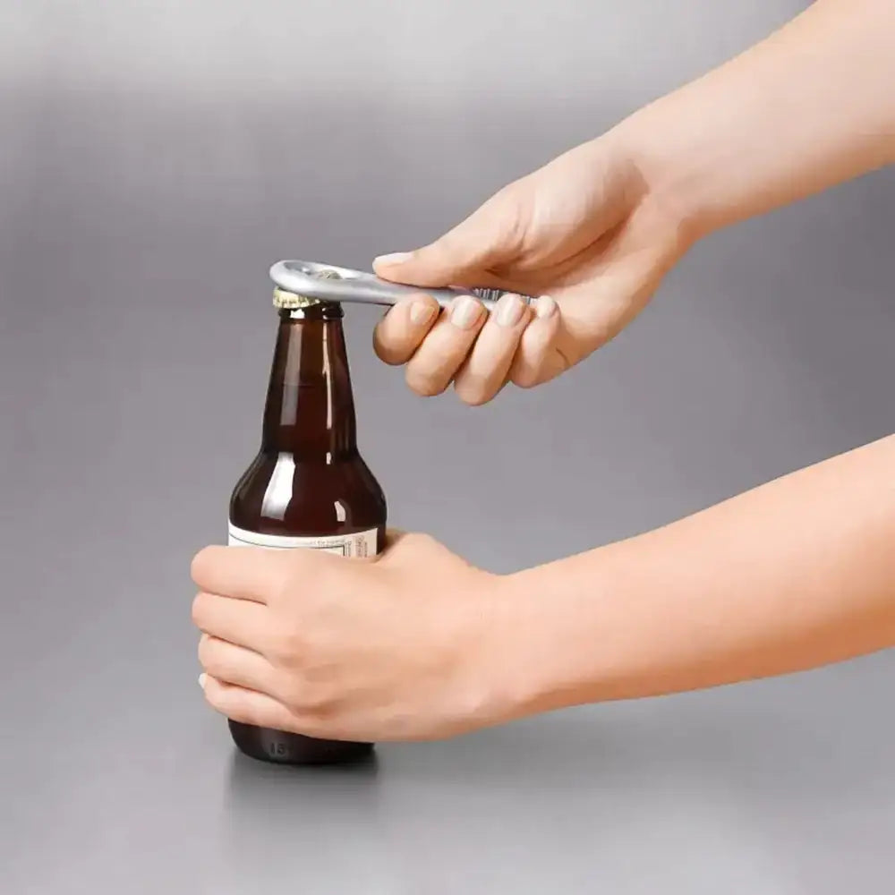 Person using a bottle opener on a beer bottle against a gray background