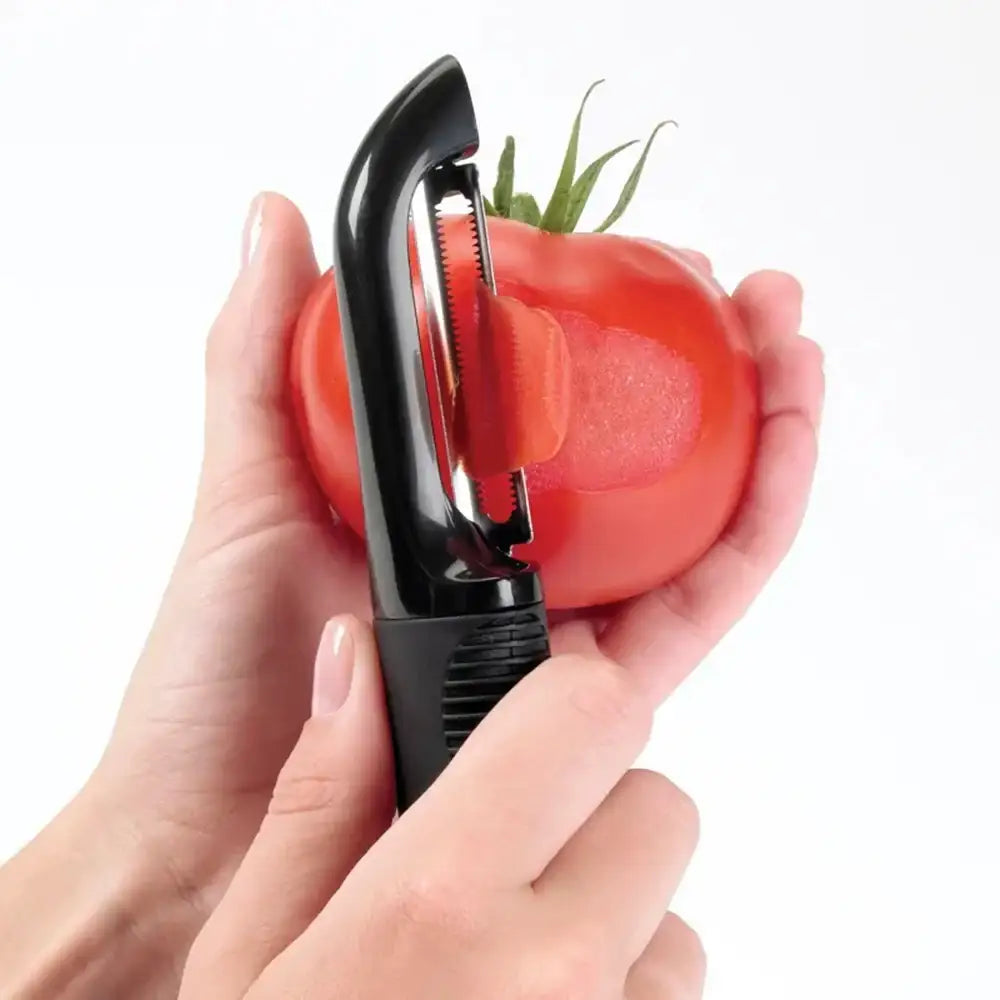 Person using a tomato peeler on a red tomato with a white background