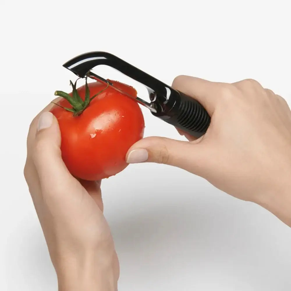 Person using a tomato peeler on a red tomato with a white background
