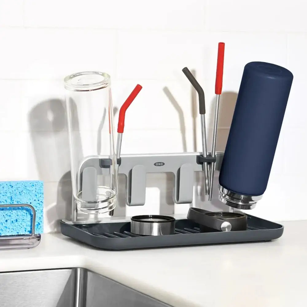 Dish drying rack with glasses, cups, and straws on a kitchen counter.