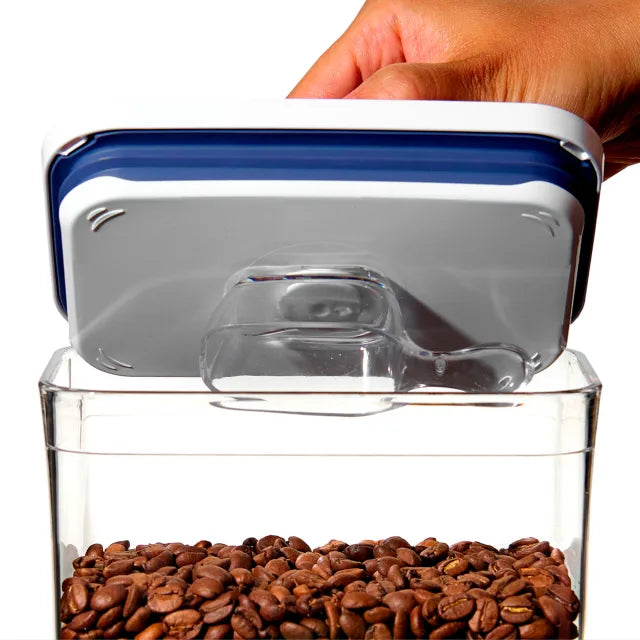 Clear container with blue lid filled with coffee beans, held by a hand.