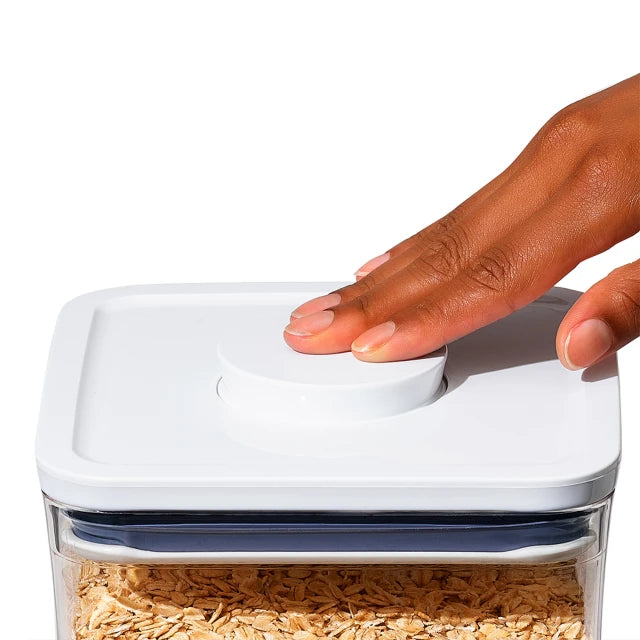 Hand opening a white container filled with oats on a white background