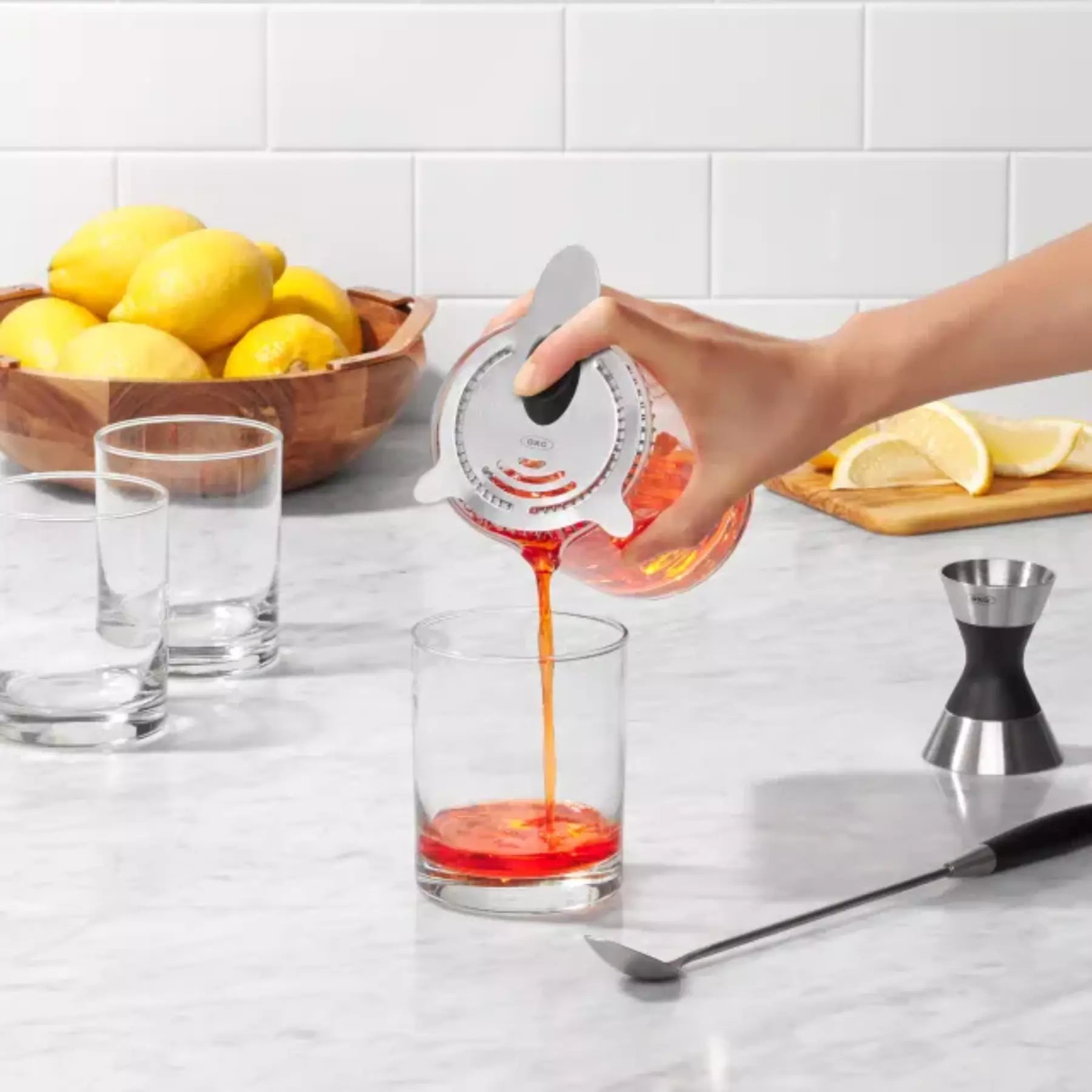 Person pouring a red liquid from a measuring device into a glass on a kitchen counter.