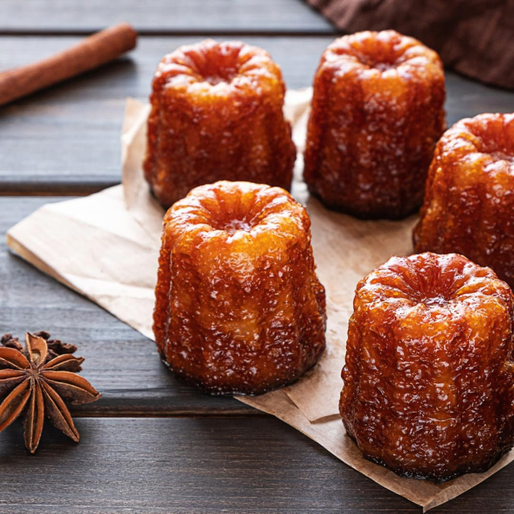 Caneles on a wooden surface with cinnamon sticks and star anise.