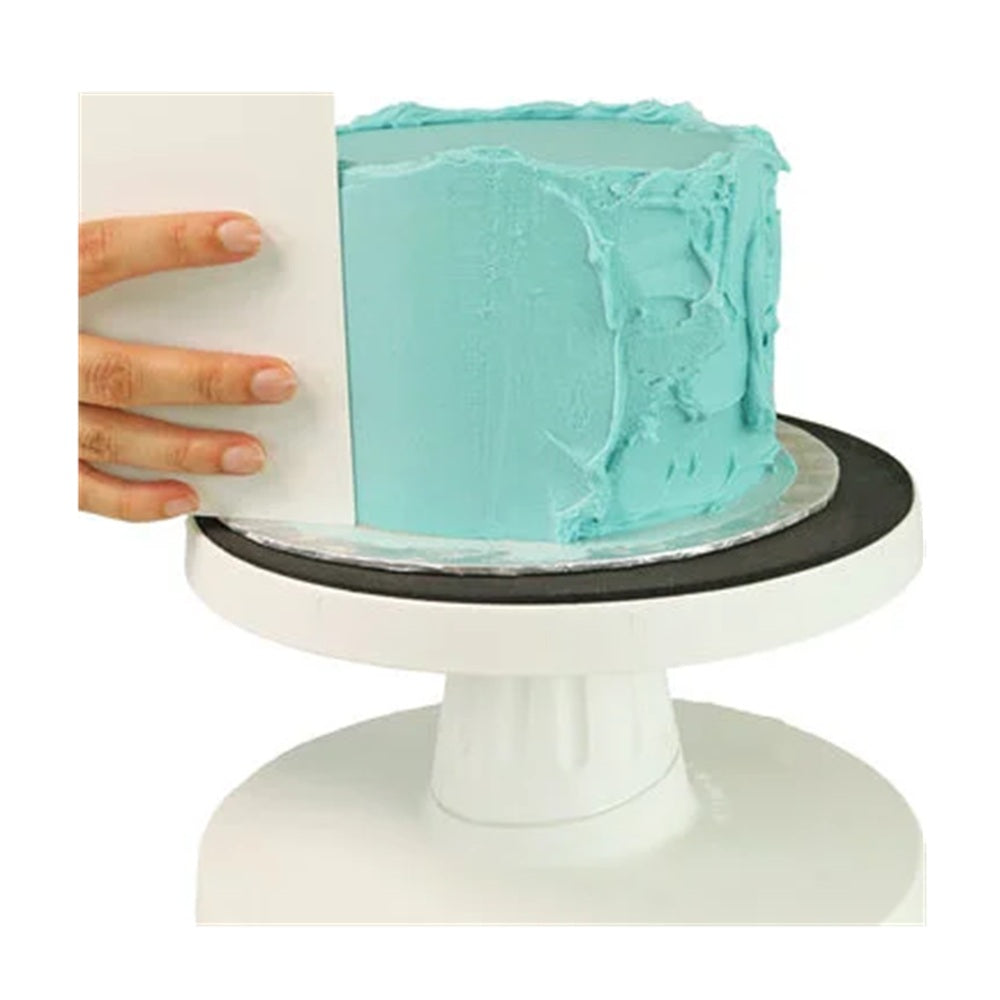 Cake being frosted on a white cake stand with a person's hand holding a spatula.