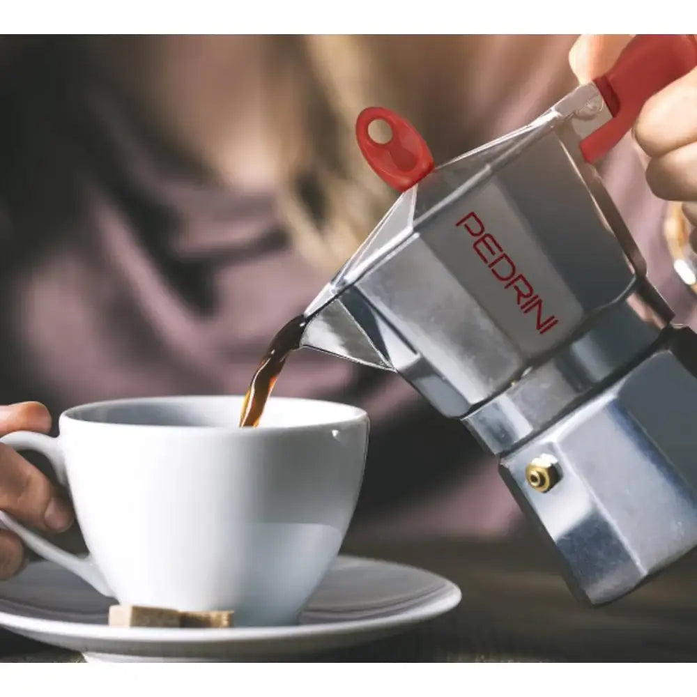 Person pouring coffee from a Pedrini espresso maker into a white cup.