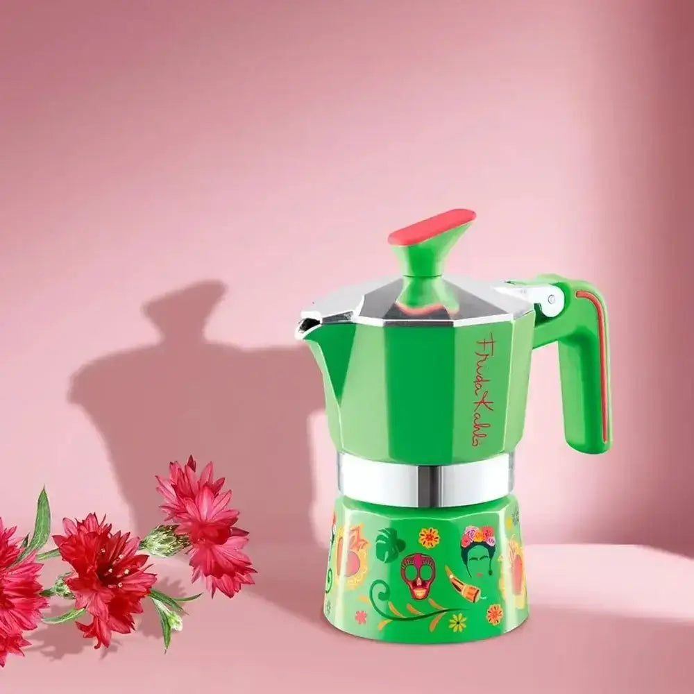 Green and red coffee maker with floral design on a pink background