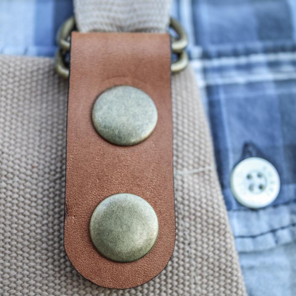 Close-up of a leather strap with metal buttons on a textured surface.