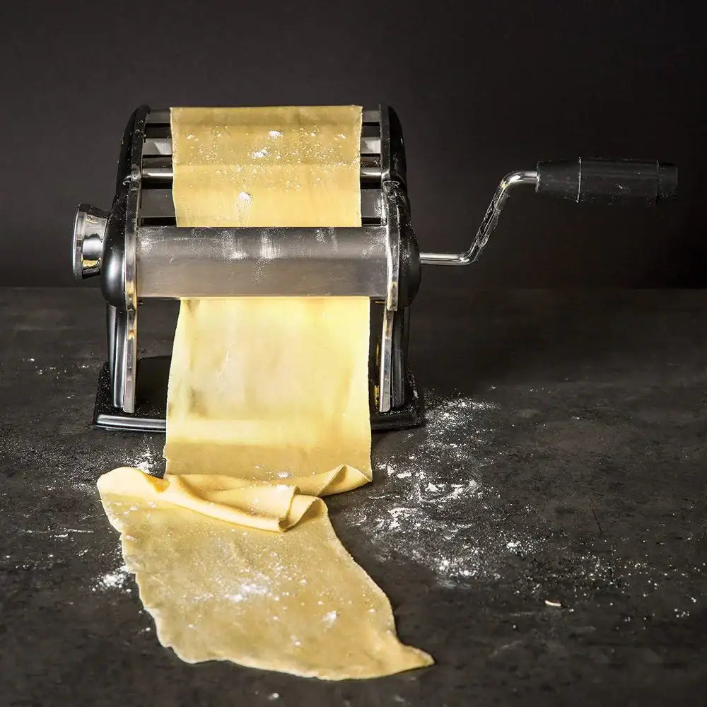 Pasta maker rolling out pasta sheets on a dark surface