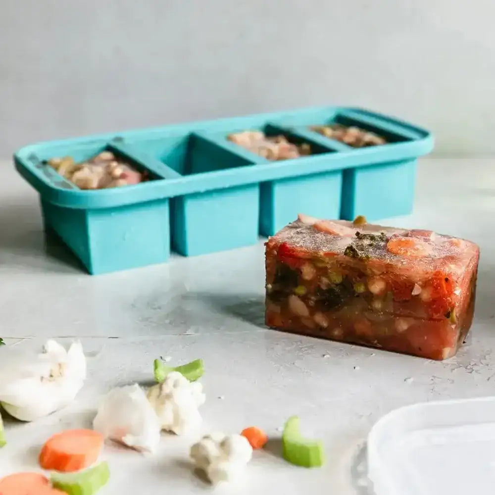 Frozen vegetable block in front of a blue silicone mold on a light surface.