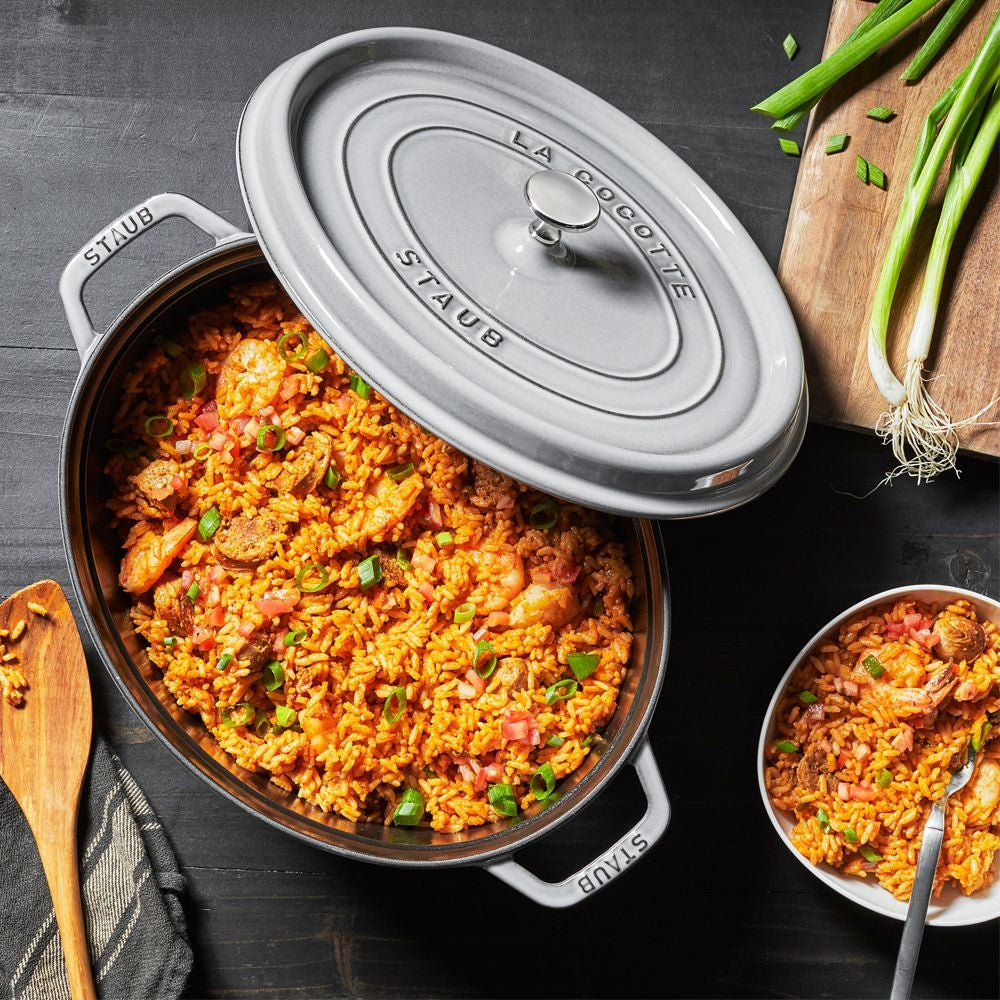 Staub cookware with a dish of colorful rice and vegetable mixture on a dark surface.