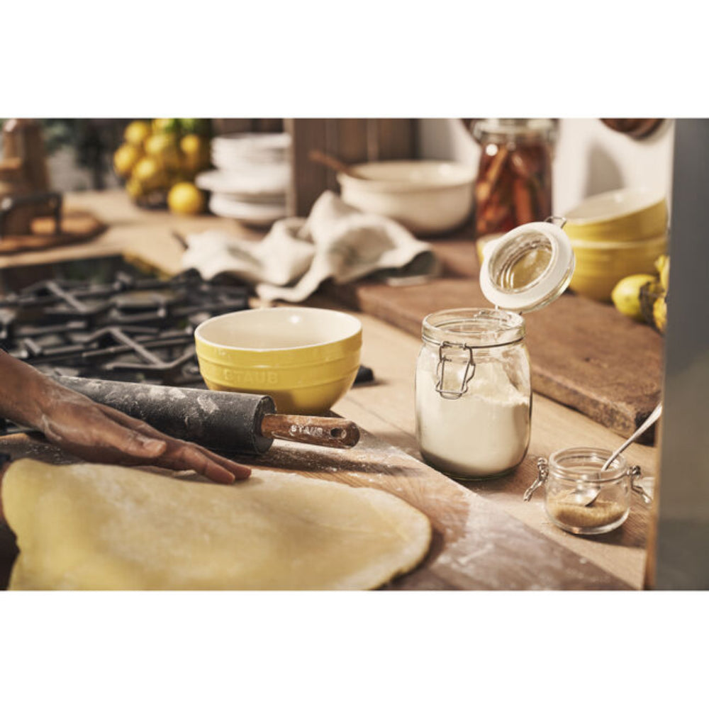 Person rolling out dough on a wooden surface with kitchen items around