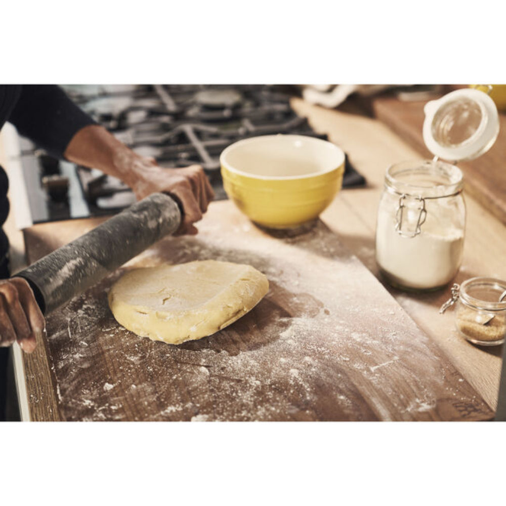 Person rolling out dough on a floured surface with kitchen items in the background.