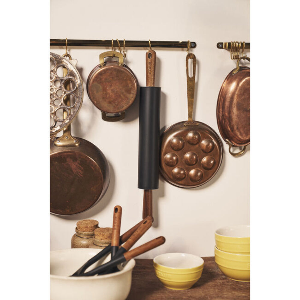 Collection of copper cookware and kitchen utensils hanging on a wall rack.