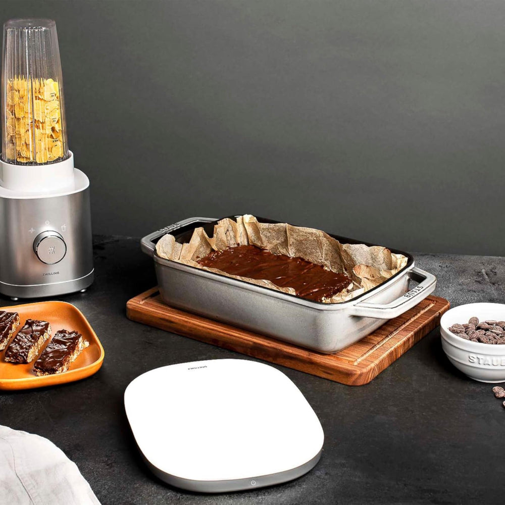 Blender, baking dish with chocolate mixture, and ingredients on a dark surface