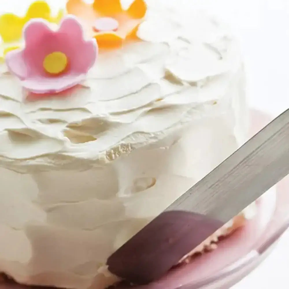 Close-up of a cake with white frosting and decorative flowers, with a knife partially inserted.