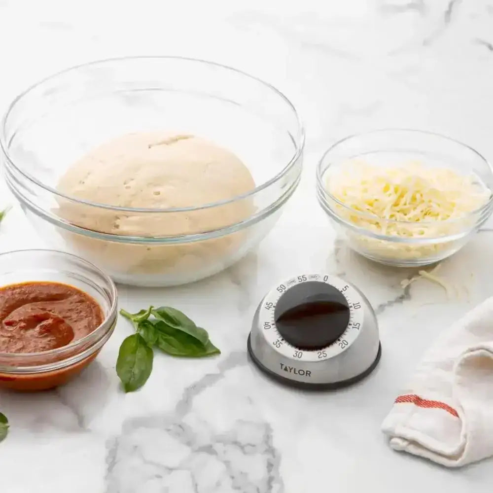 Bowl of pizza dough, sauce, cheese, and basil with a Taylor timer on a marble surface.
