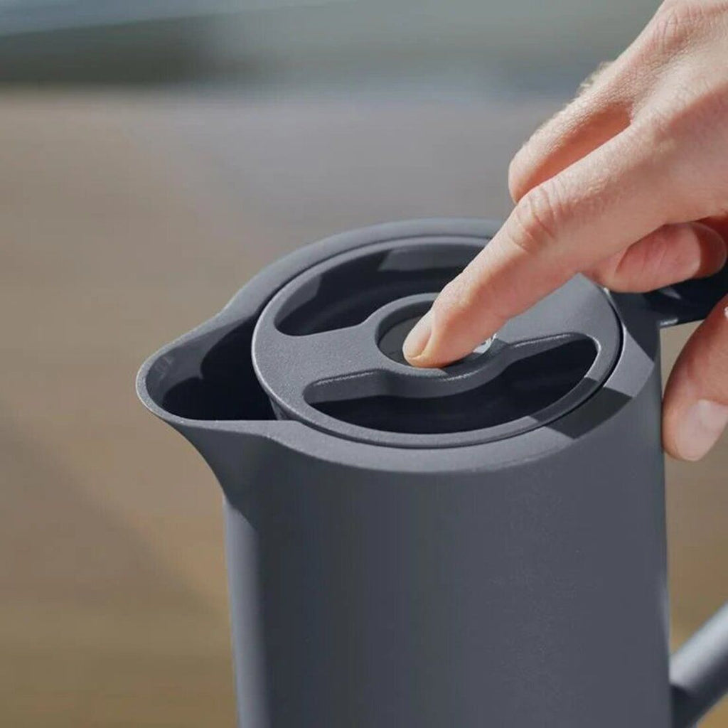 Person pressing a button on a gray pitcher with a blurred background