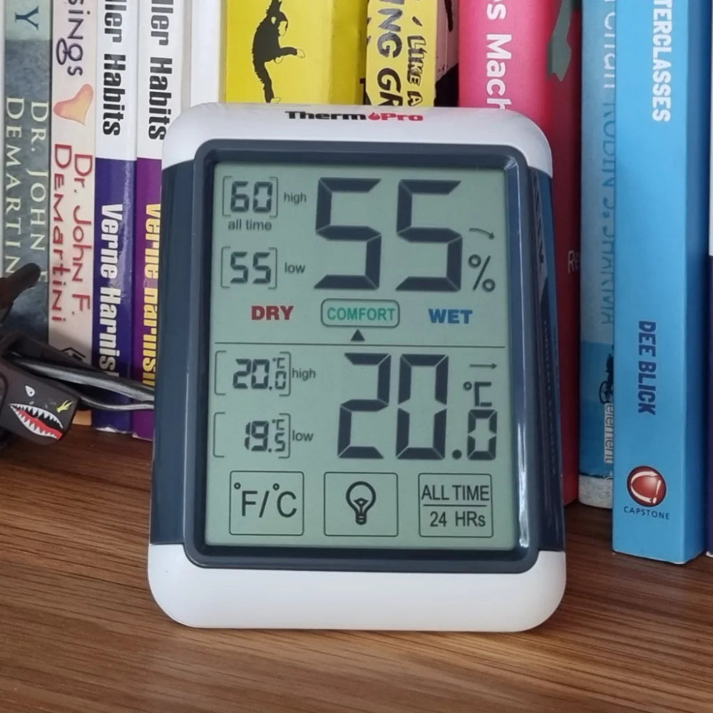 Digital thermometer with humidity and temperature display on a bookshelf background