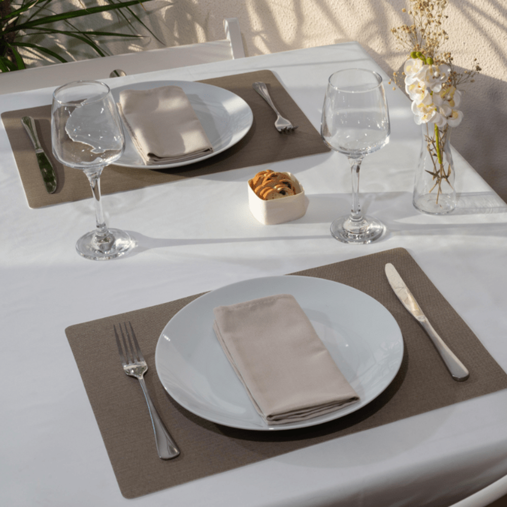 Dining table setting with plates, glasses, and cutlery on a white tablecloth.