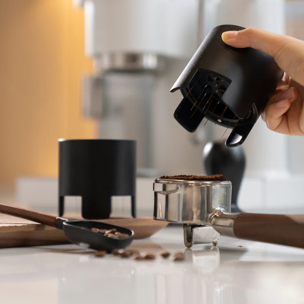 Hand using a coffee distributor tool to loosen ground coffee in portafilter