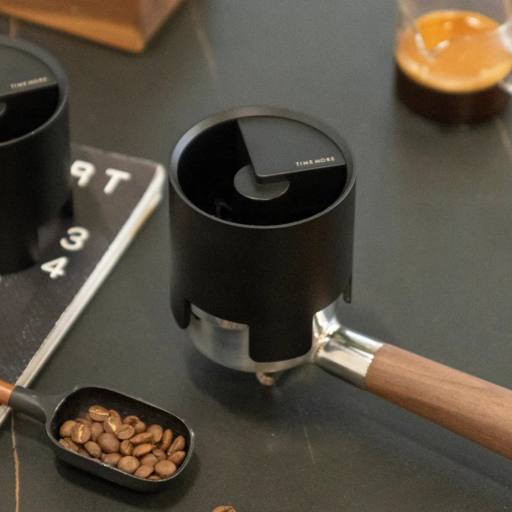 Black Timemore coffee distributor tool with coffee beans on a dark surface