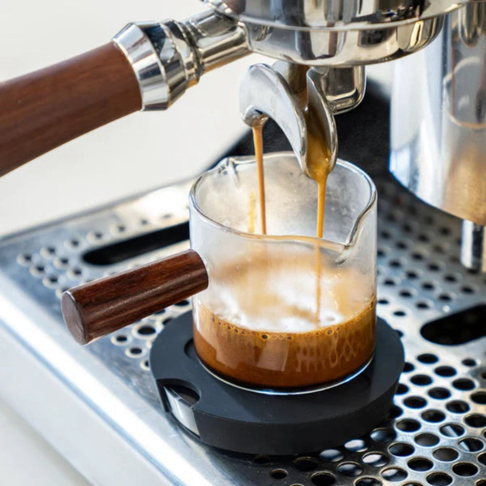 Espresso pouring from a portafilter into a glass espresso cup on a coffee machine.