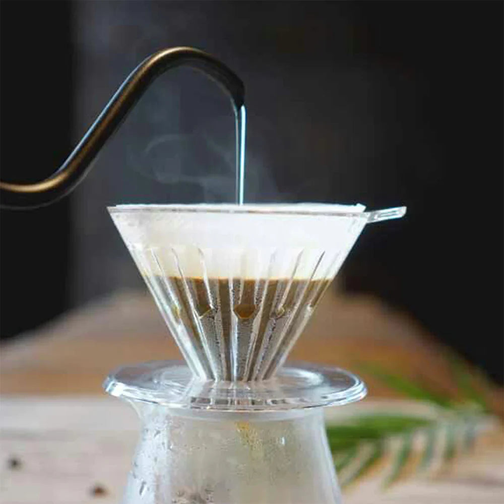 Coffee brewing process with a glass carafe and paper filter on a wooden surface.