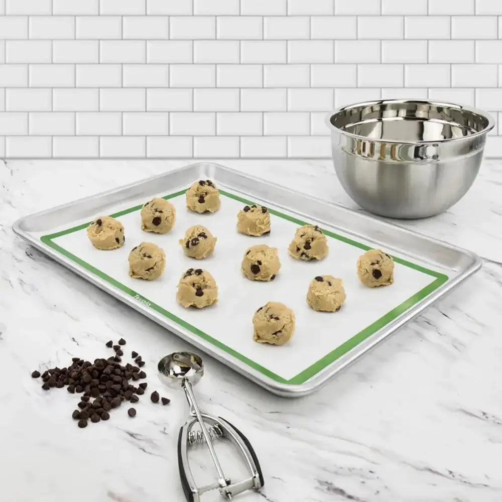 Baking tray with cookie dough balls, chocolate chips, and a mixing bowl on a marble countertop.