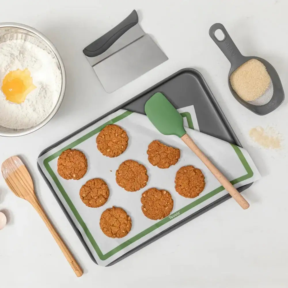 Baking tray with cookies, spatula, and measuring cup on a white surface