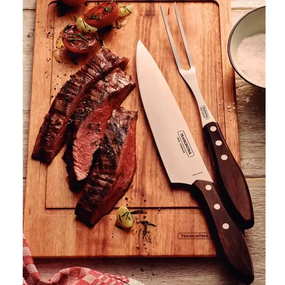 Wooden cutting board with sliced steak, a knife, and fork on a wooden surface.