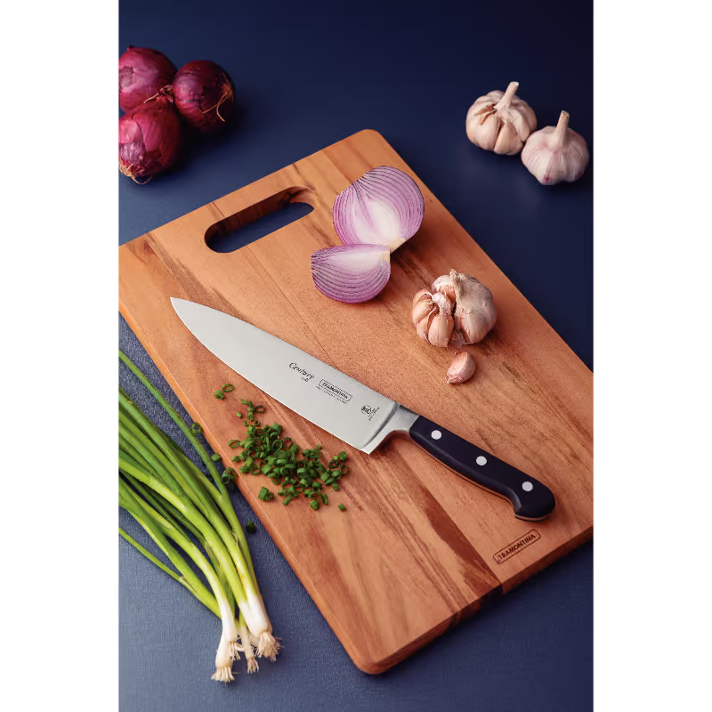Wooden cutting board with a chef's knife, chopped onions, garlic, and green onions on a dark blue background.