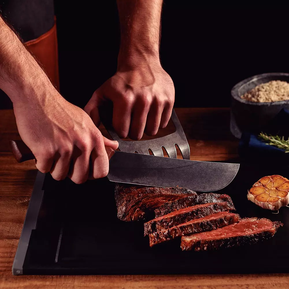 Person slicing cooked meat on a cutting board with a knife.