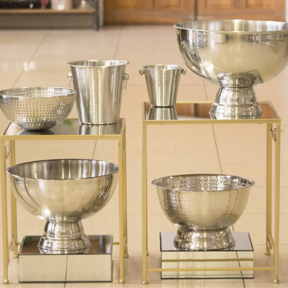 Set of silver bowls and buckets on gold stands against a tiled wall.