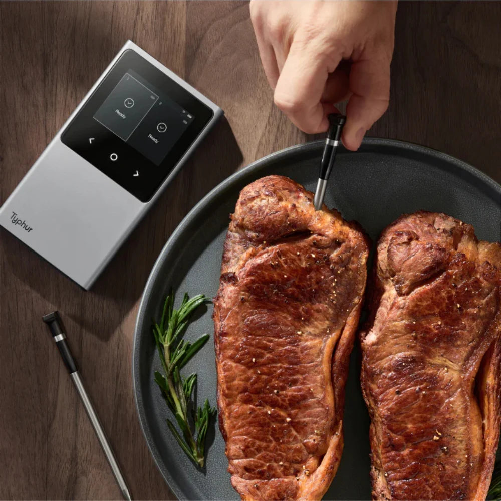 Two pieces of cooked meat on a plate with a digital thermometer next to it on a wooden surface.