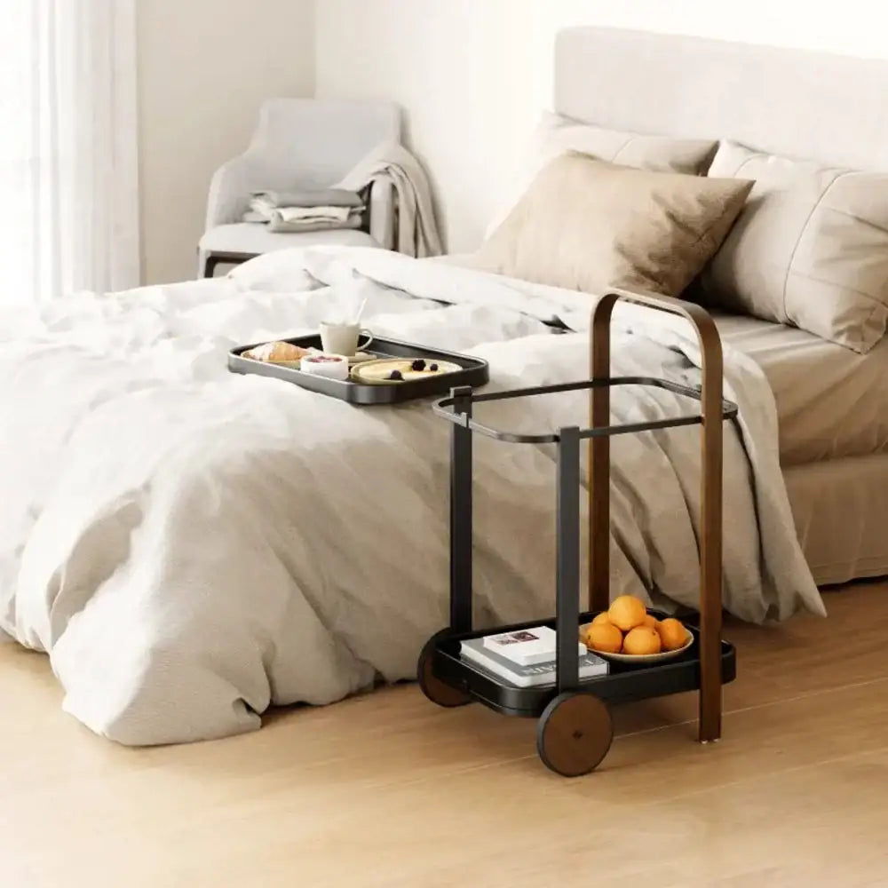 Black serving cart with a tray on a bed in a bedroom setting